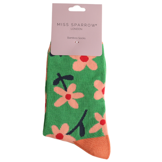 A pair of green bamboo and cotton socks with an orange toe and a floral pattern, displayed with a Miss Sparrow London label.