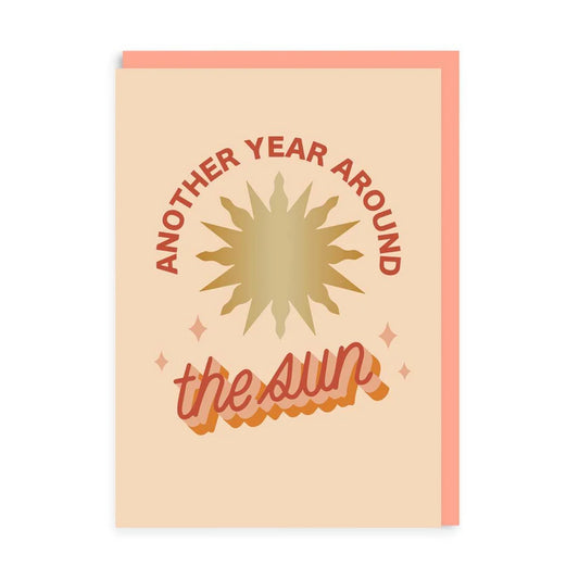 Greeting card featuring gold foil lettering with the phrase Another year around the sun and a stylised sun illustration on a beige background.