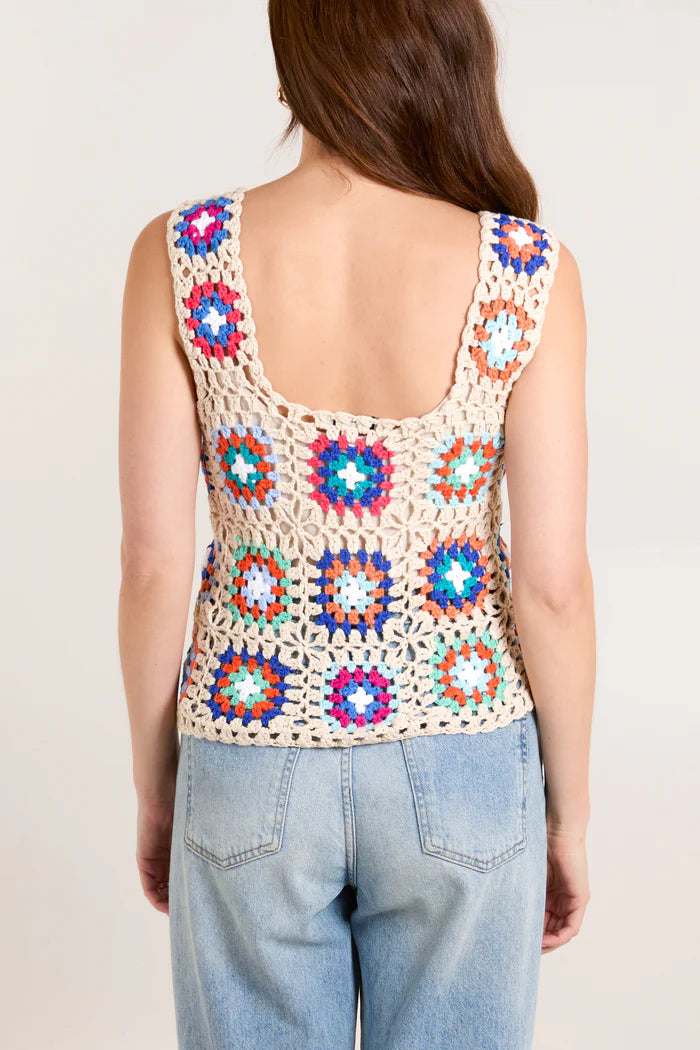A trendsetting woman wears a sleeveless crochet top featuring colourful patchwork, paired effortlessly with light blue jeans, seen from the back.