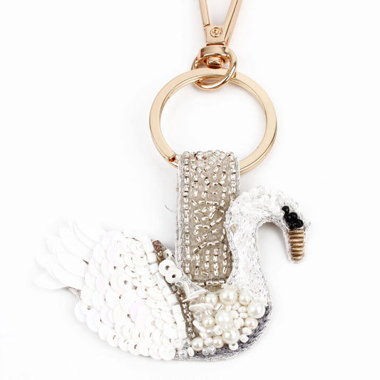 A handcrafted swan keyring adorned with white sequins, glass beads, and intricate silver embroidery, all elegantly attached to a gold ring fastener.