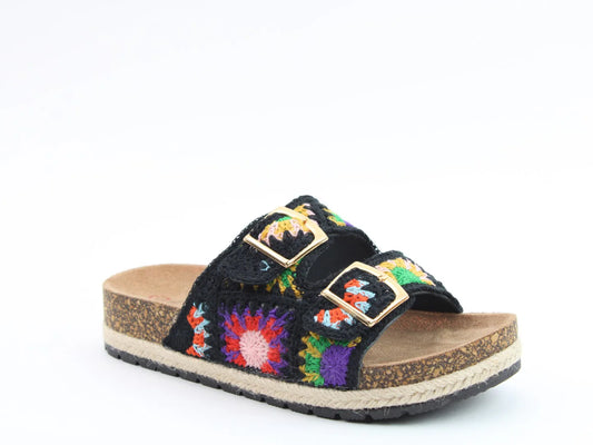 A black, vegan-friendly sandal with a colourful stitched upper, two gold buckles, and a cork sole with a black rubber outsole, displayed against a white background.