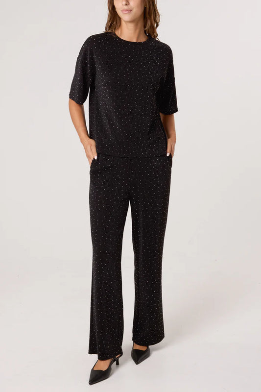 Person standing against a plain background wearing a black trouser suit with a small white spot pattern, paired with black pointed-toe shoes—a stylish festive outfit.