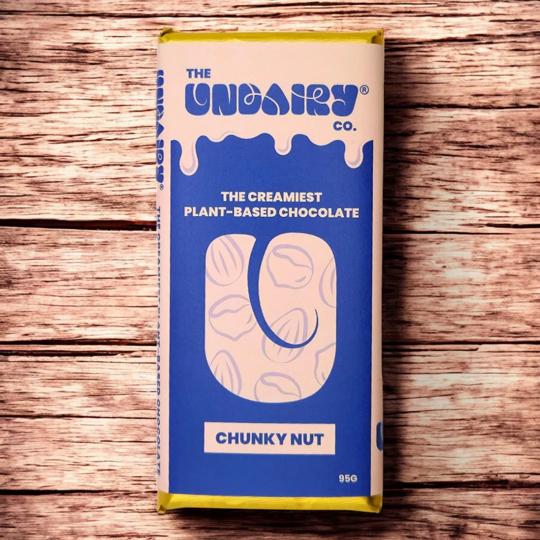 A blue and cream-coloured chocolate bar labelled The Creamiest No Dairy Chocolate – Chunky Nut from The UnDairy Co. offers a vegan twist, placed on a wooden surface.