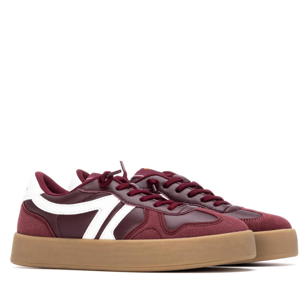 A pair of maroon low-top vegan trainers with white side stripes, maroon laces, and tan gum soles, shown on a white background.