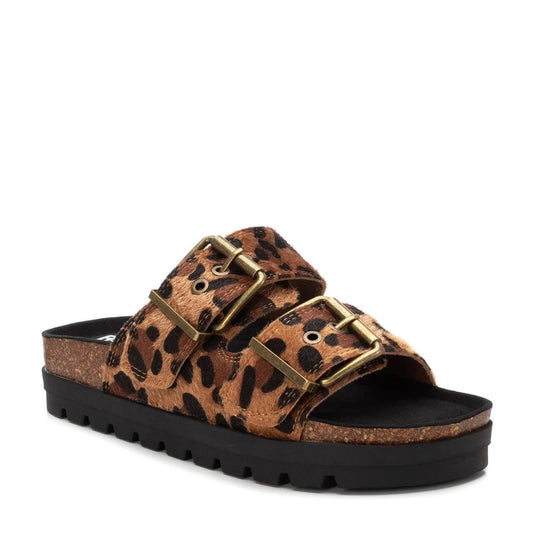 A slip-on sandal crafted from vegan leather, featuring two animal print straps with gold buckles, a cork footbed, and a black textured sole. PETA certified for eco-conscious style.