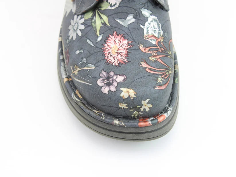 Close-up of the toe of a dark-coloured boot with a floral print, displaying an intricate, multicoloured pattern on a white background.