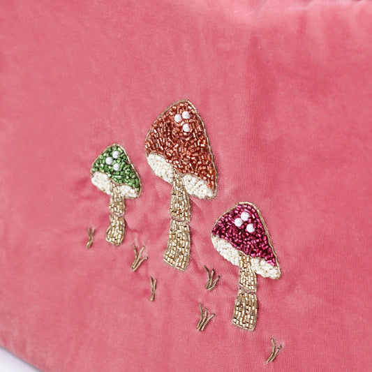 Pink velvet pouch adorned with embroidered mushrooms in green, brown, and red, featuring intricate glass beads on the caps and stems, with delicate grass details underneath; lovingly hand-made in India.