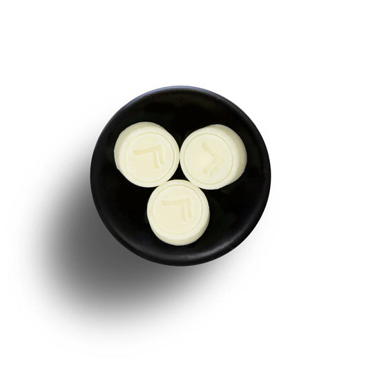 Three cream-coloured round discs, each a Vegan Wax Melt, rest in a black bowl on a white background.