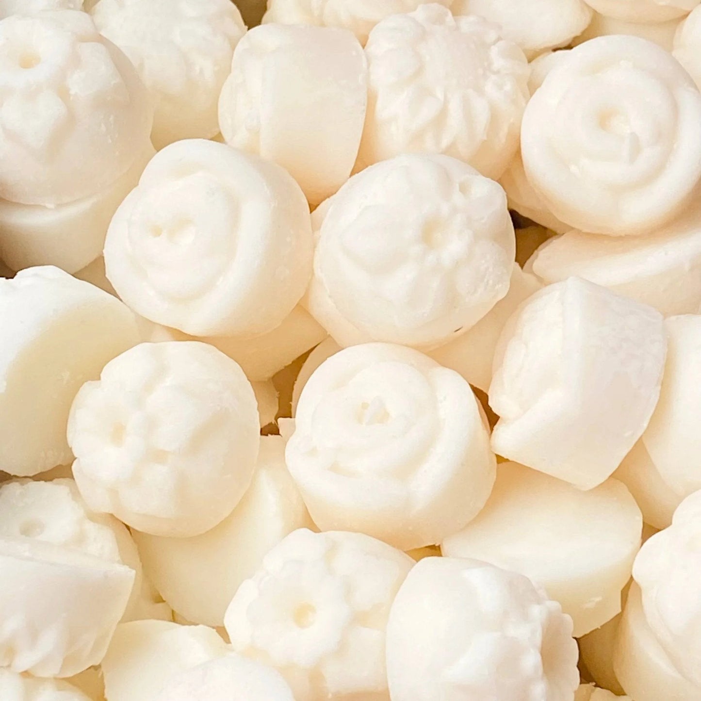 A pile of small, white, round bath bombs, each adorned with different floral and geometric patterns on the surface, nestled beside a vibrant Bergamot Verbena wax melt that fills the air with calming aromas.