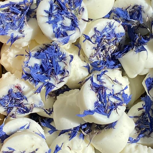 White wax melts infused with the fresh scent of clean laundry are topped with scattered dried blue petals, all elegantly packaged in recyclable packaging.