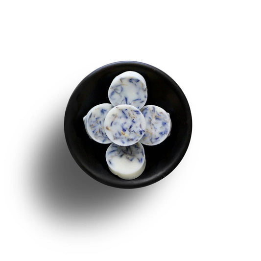 In a black bowl against a white background, five round white Clean Laundry wax melts adorned with blue flower petals display their natural wax.