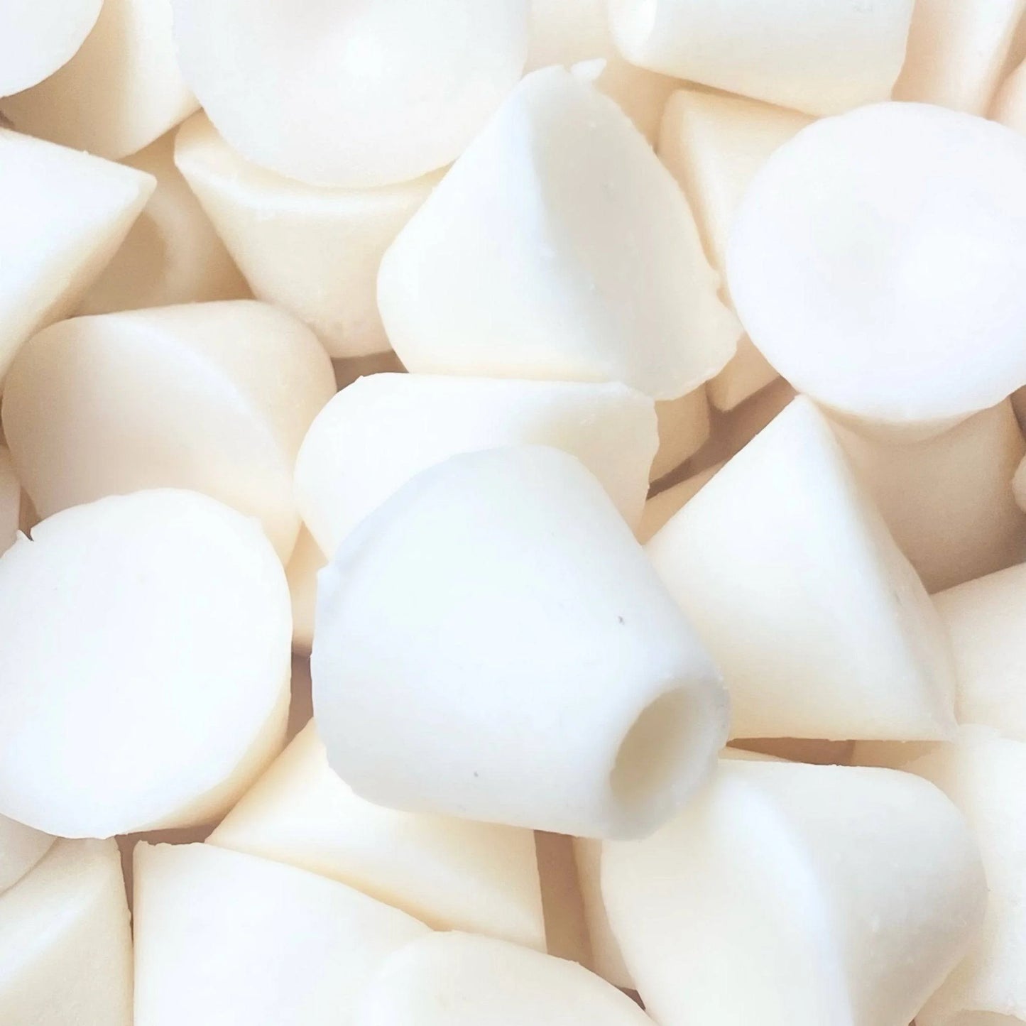 Close-up of a pile of cylindrical vegan soya wax melts with a hollow top, infused with Coconut & Sea Salt, arranged randomly in soft lighting.