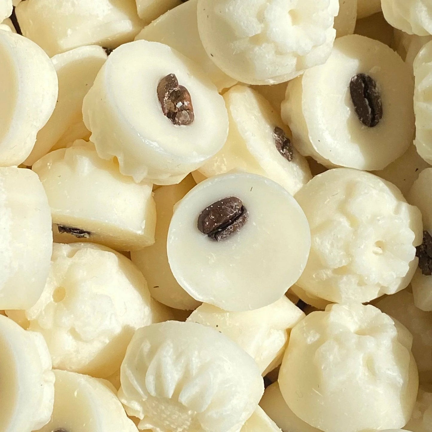 A pile of white circular chocolates, each with a single coffee bean embedded in the centre, offers a tasteful delight thats vegan-approved for an environmentally friendly treat.