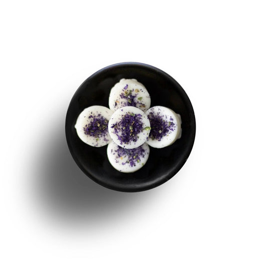Five white macarons with purple sprinkles sit in a black bowl on a white surface, exuding an air of elegance reminiscent of a Floral Oud Wax Melt.