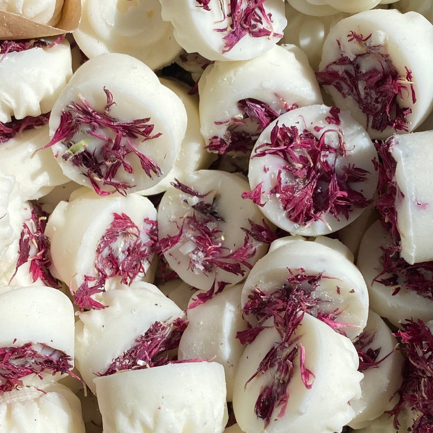 White confections topped with dried purple flowers are closely arranged, creating a textured and colourful display, reminiscent of a Floral Oud Wax Melt experience.