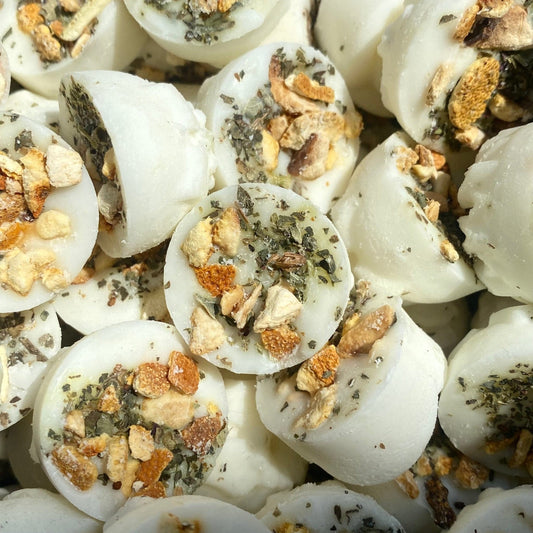 Round white wax melts made from natural soya wax, adorned with bits of orange peel and green herbs such as basil, gathered together. Enjoy the fresh fragrance of Orange, Lime & Basil in a vegan-friendly form.