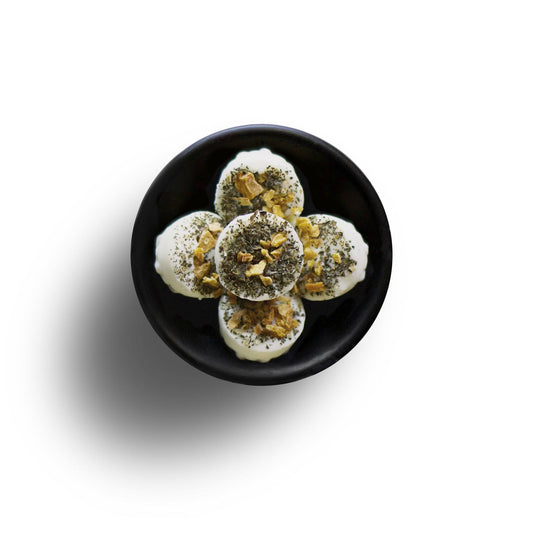 A black plate with round yoghurt bowls, topped with chia seeds and crushed nuts, viewed from above. The meal, alongside an Orange Lime & Basil Soya Wax Melt, casts a playful shadow—a vegan-friendly delight.