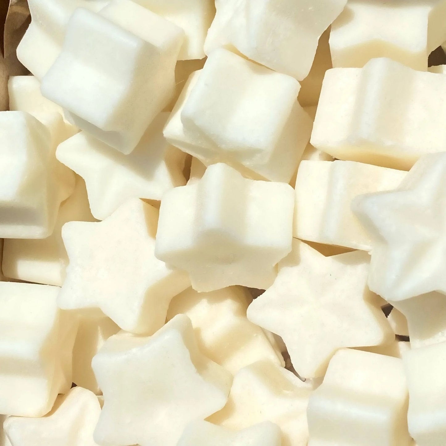 A collection of star-shaped and square-shaped white marshmallows, reminiscent of vegan wax melts, viewed from above and closely packed together.