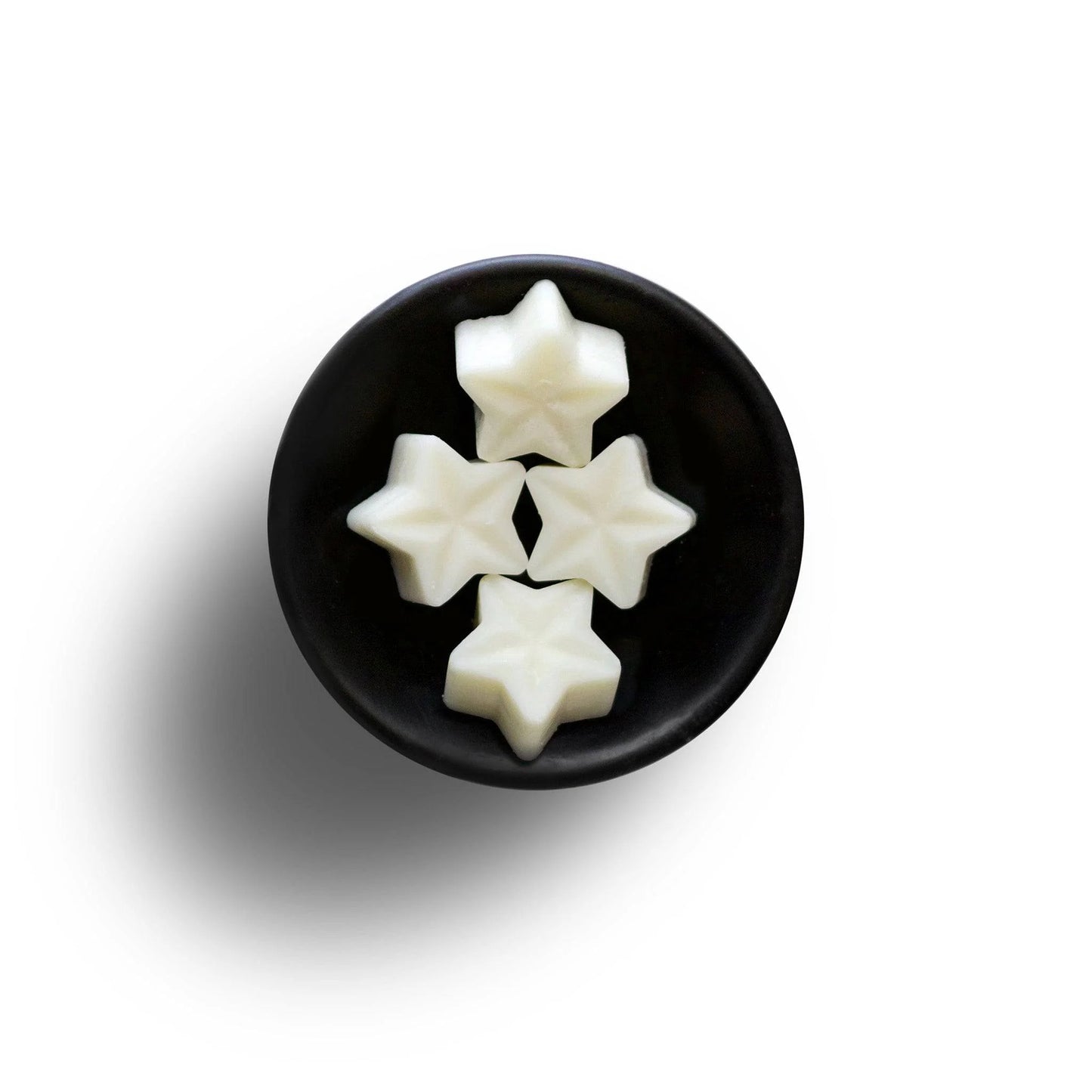 Four star-shaped white sweets in a black bowl on a white background, elegantly reminiscent of vegan wax melts.
