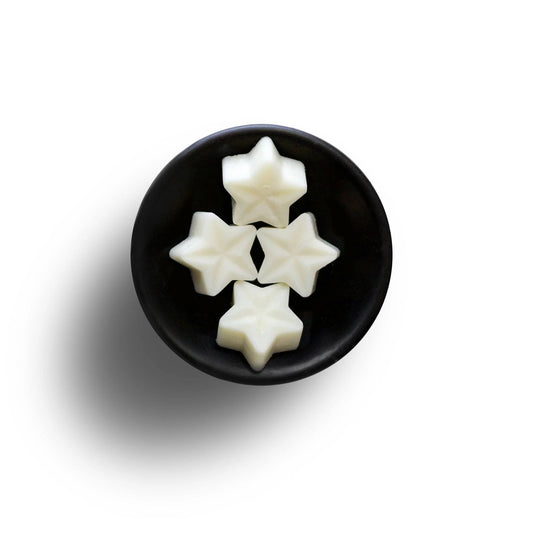 Four star-shaped white sweets in a black bowl on a white background, elegantly reminiscent of vegan wax melts.