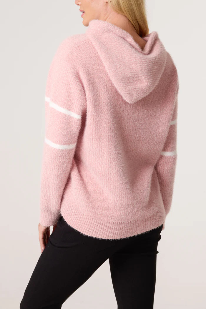 A person wearing a baby pink hoodie with white stripes on the sleeves and black trousers, seen from behind.