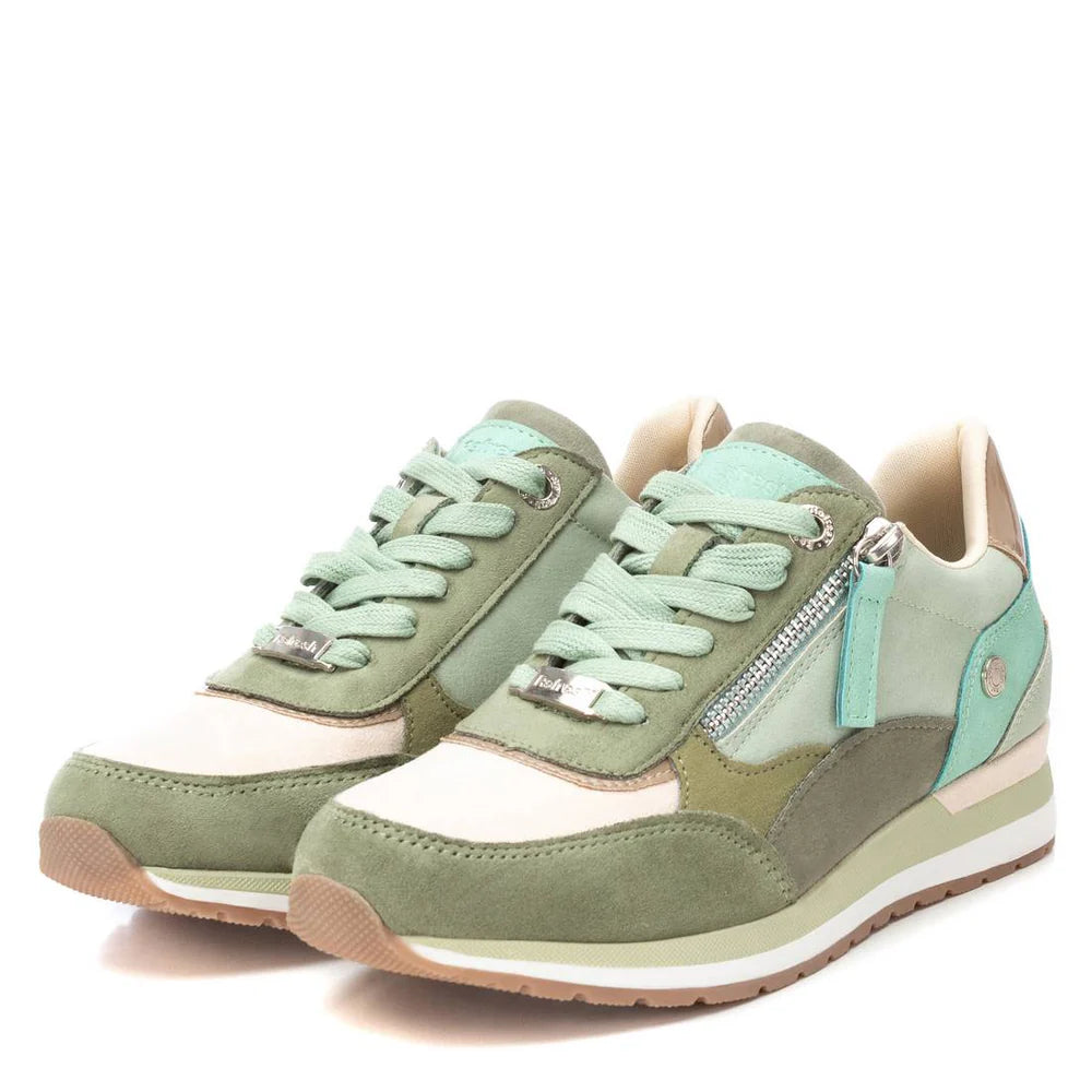 A pair of green and beige vegan-friendly trainers in suede and fabric, featuring light green laces, side zips, and beige rubber soles, displayed against a white background.