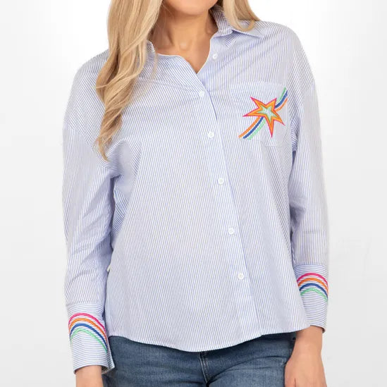 The person is wearing a Beau Long Sleeve Shirt with a colourful starburst design on the chest and rainbow-striped cuffs, stylishly paired with jeans.