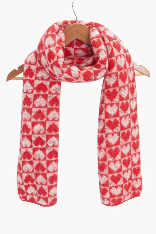 A Red Heart Vegan Scarf featuring a repeating heart pattern hangs on a wooden hanger, providing a cosy and cruelty-free scarf choice set against a plain background.