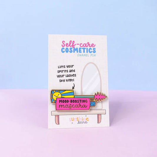 A colourful enamel mascara pin labelled Mood-Boosting Mascara rests on a card featuring Self-care Cosmetics and a mirror illustration, making it the ideal self-care gift.