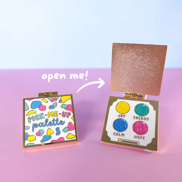 Two colourful square compacts are shown—one closed, labelled Pick-Me-Up Palette enamel pin, and one open, displaying four glittery shades named Joy, Energy, Calm, and Hope; a perfect self-care gift.