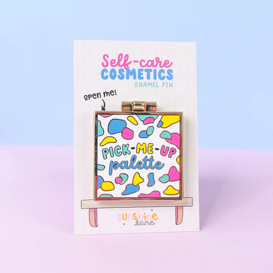 A colourful eyeshadow palette pin reads "Pick-Me-Up Palette" and is attached to a Self-care Cosmetics card, set against a pastel blue and pink background—perfect as a self-care gift.