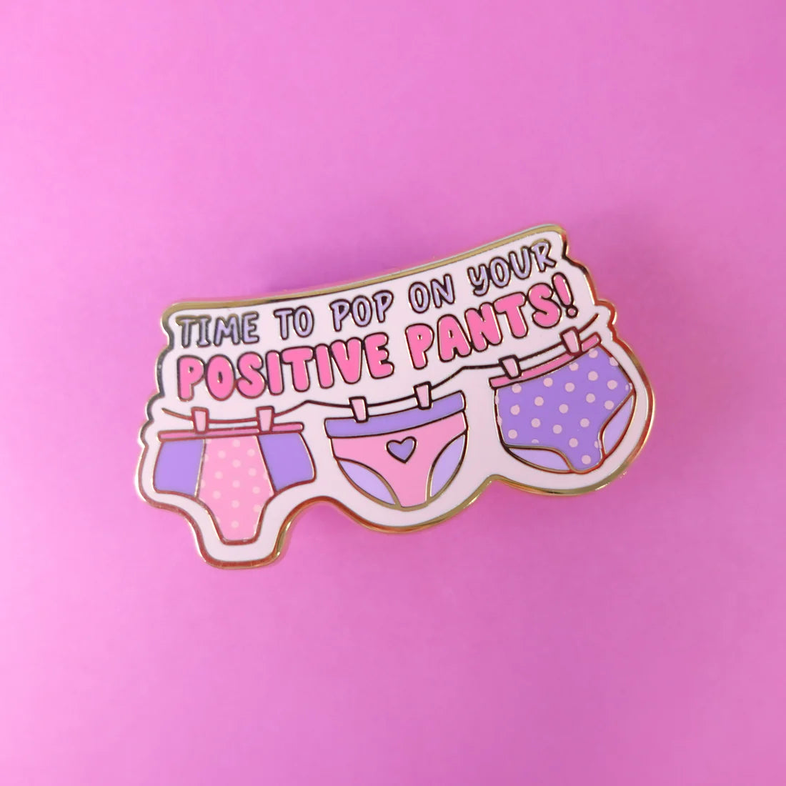 A cheerful enamel pin featuring three pairs of cartoon pants on a washing line and the text “Time to pop on your positive pants!”—an uplifting gift for anyone in need of a bit of encouragement.