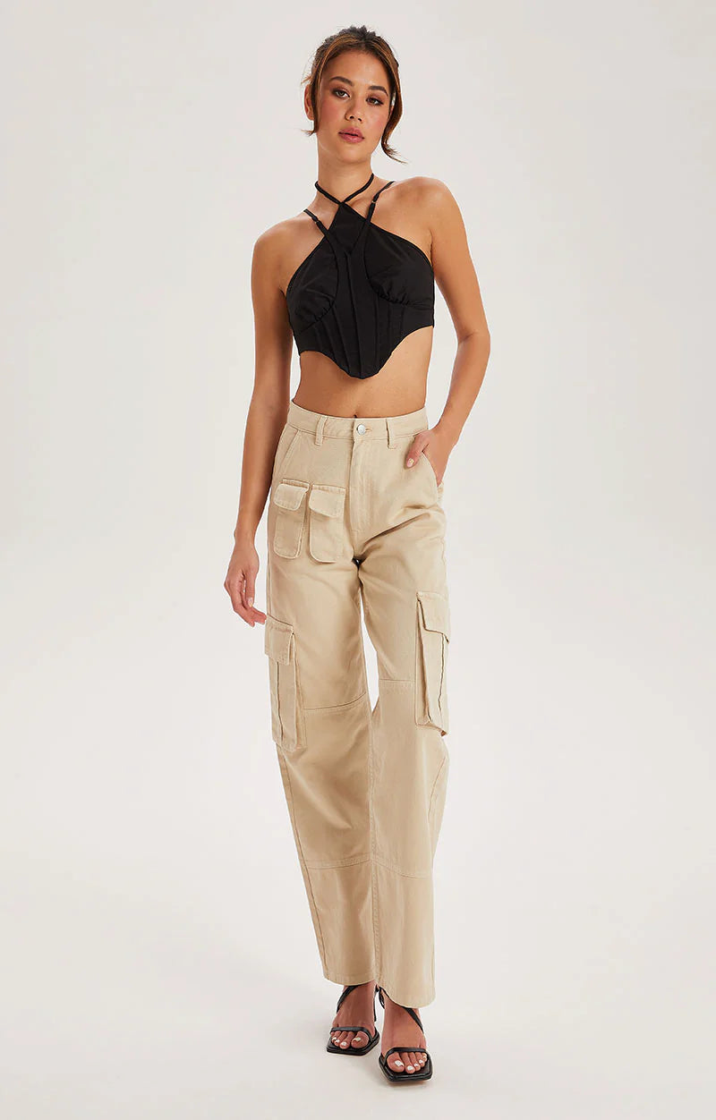 A woman stands wearing a black halter crop top, high-waisted Off White cotton cargo trousers with pockets, and black heeled sandals against a plain background.