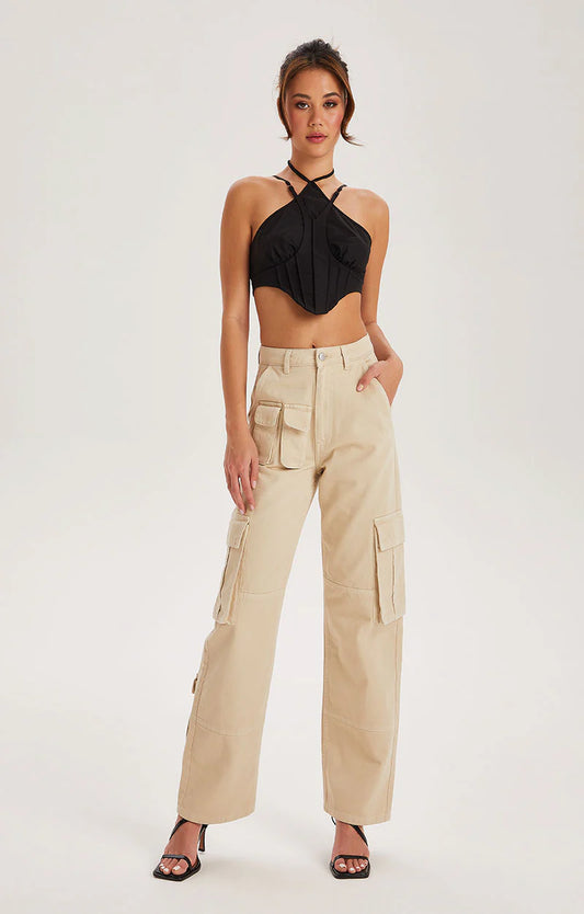 A woman stands facing forward in a black halter crop top, off-white cotton cargo trousers with a high waist and pockets, and black heeled sandals against a plain white background.