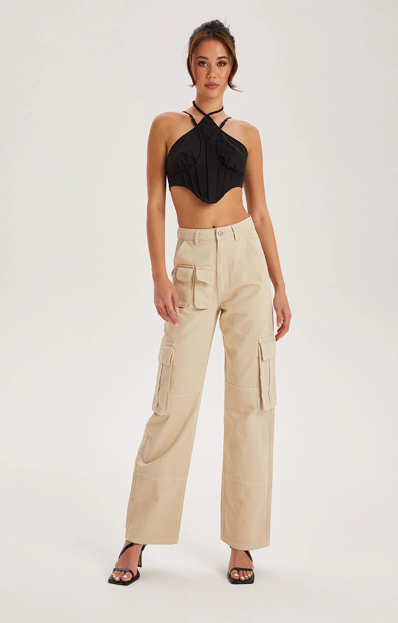 A woman stands against a plain background wearing a black halter crop top, high-waisted Off White cotton cargo trousers with a five-pocket denim silhouette, and black heeled sandals.