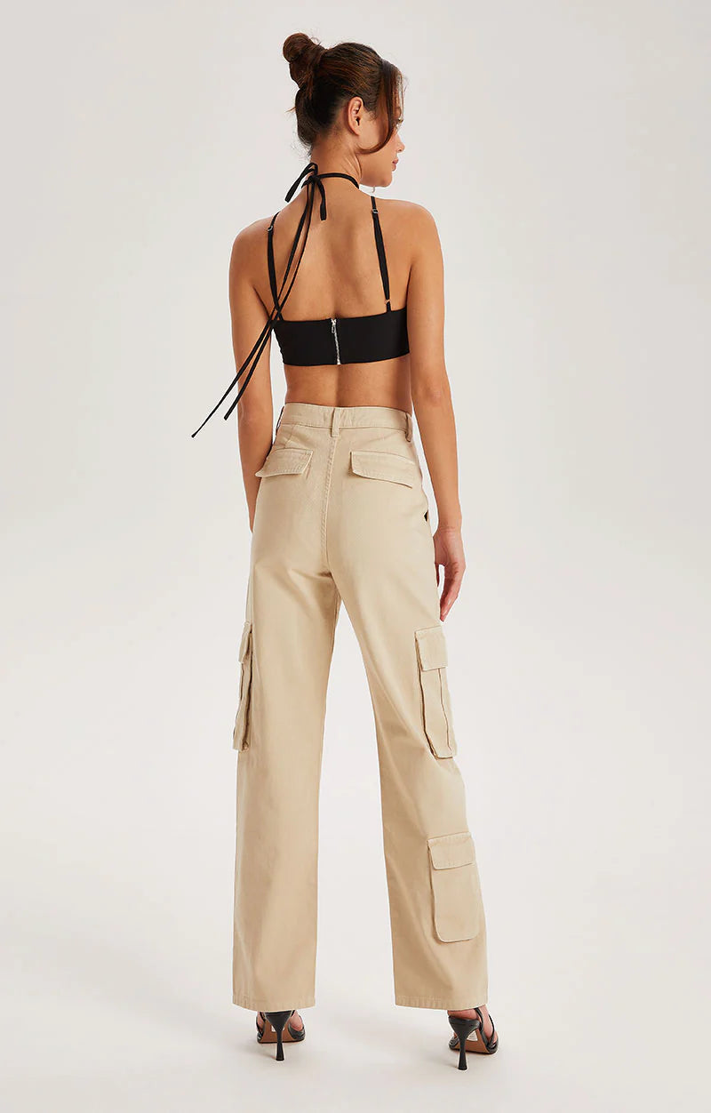 A woman stands with her back to the viewer, wearing a black halter crop top, Off White cotton cargo trousers featuring a high waist and a five-pocket denim silhouette, paired with black heeled sandals against a plain background.