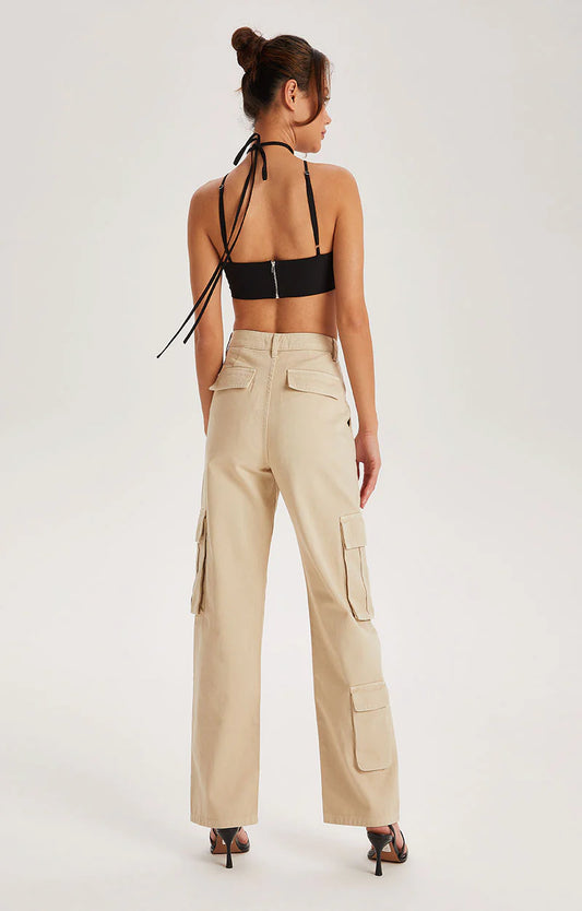 A woman stands with her back to the viewer, wearing a black halter crop top, Off White cotton cargo trousers featuring a high waist and a five-pocket denim silhouette, paired with black heeled sandals against a plain background.
