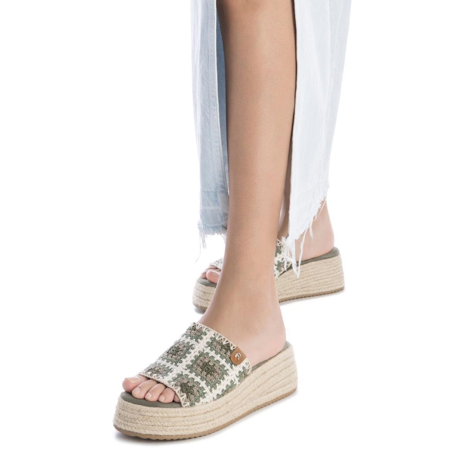 A person wearing light blue frayed hem trousers and platform sandals featuring a green and white woven pattern.