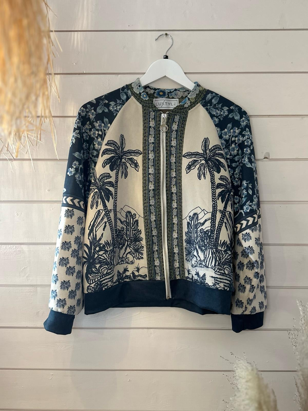A patterned jacket with palm tree and floral designs in black and cream tones hangs on a white, wall-mounted hanger.