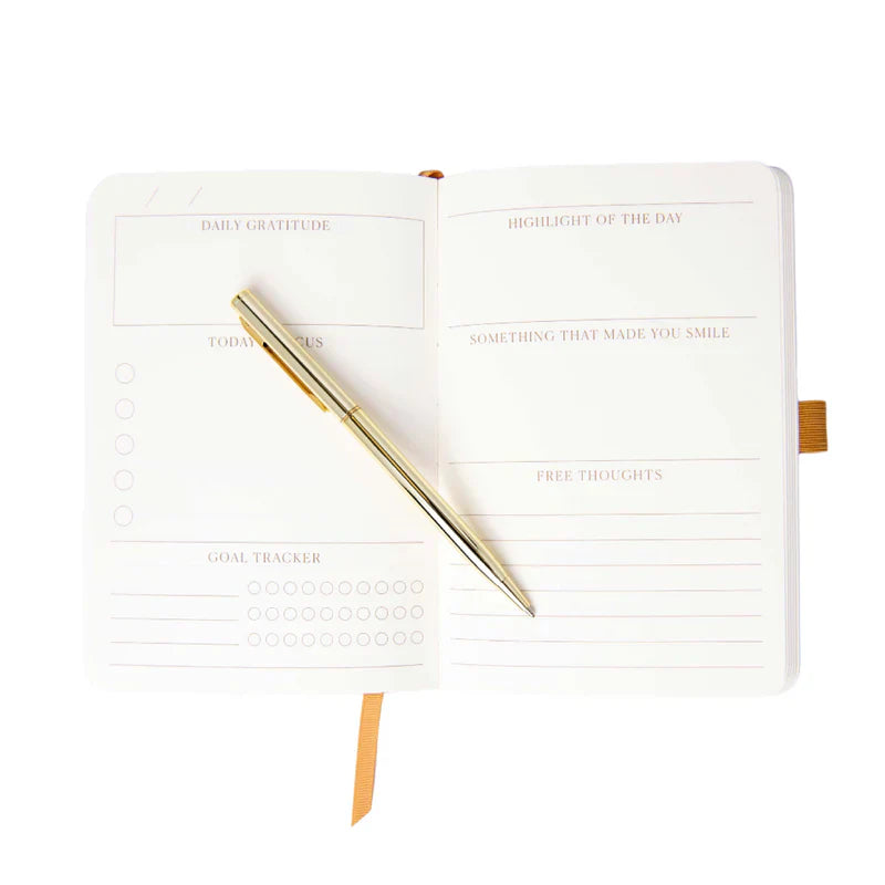 An open diary with labelled sections and a gold pen resting on its pages. Sections feature daily gratitude, goals, highlights, and free thoughts.