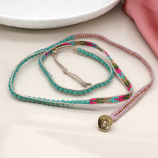 Three beaded bracelets are arranged on a glossy surface. One is turquoise, another is a statement piece thats multicoloured with a bronze charm, and the third is pink with colourful beads.