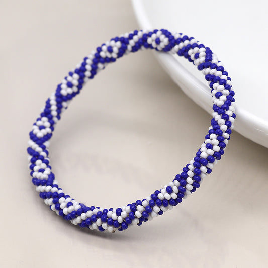 A hand-crafted design showcases a round beaded bracelet with a blue mix diamond pattern, resting gracefully near a white dish on a light surface.