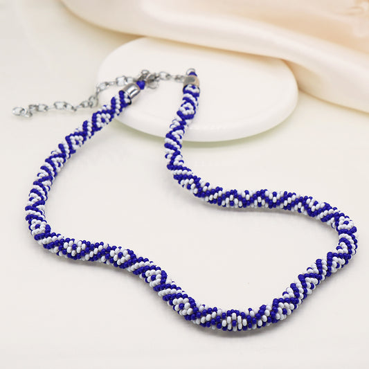 A blue and white bead necklace with a snake-inspired spiral design is elegantly displayed on a white surface.