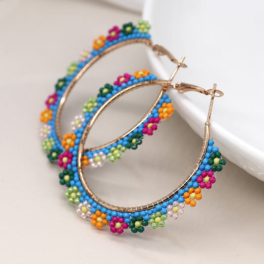 Hoop earrings inspired by florals, adorned with multicoloured beads and small beaded flowers in vibrant hues, resting on a neutral surface.