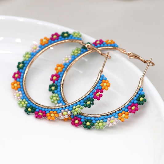 Floral-inspired hoop earrings with multicoloured beads in blue, green, orange, pink, and yellow are elegantly displayed on a white surface.