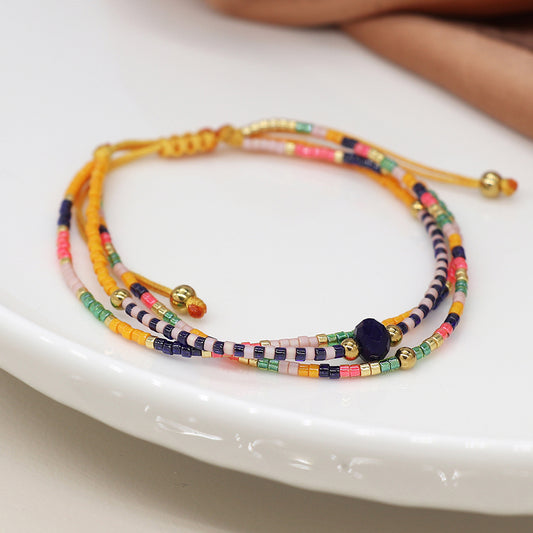 A unique, luxurious accessory, this multicoloured beaded bracelet showcases navy, coral and green beads with gold accents, elegantly displayed on a white surface.