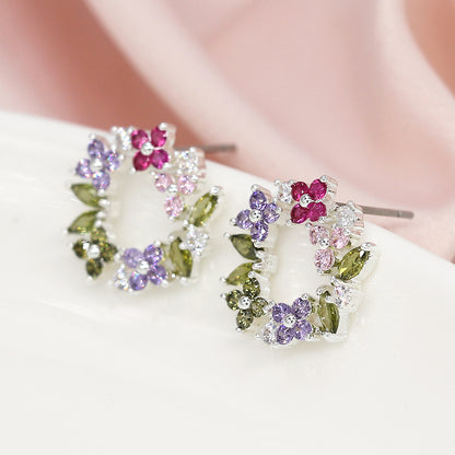 Floral Circle Studs embellished with clusters of pink, purple, and green faceted crystals set in silver, resting beautifully on a soft pink fabric background.