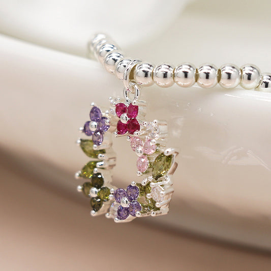 Silver necklace with a pendant featuring multicoloured gemstone clusters arranged in a circular pattern, reminiscent of a floral crystal bracelet, displayed on a white surface.