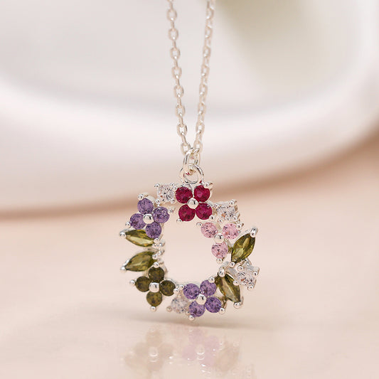 An artisanal silver necklace featuring a round, floral circle pendant embellished with clusters of faceted crystals in red, purple, pink, and green gemstones.