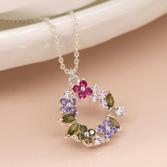 A silver chain necklace featuring a floral circle pendant embellished with faceted crystals in pink, purple, green, and clear tones, arranged in a captivating pattern.